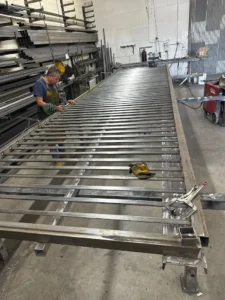 A worker assembling a very long metal gate frame.