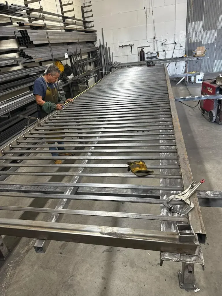 A worker assembling a very long metal gate frame.