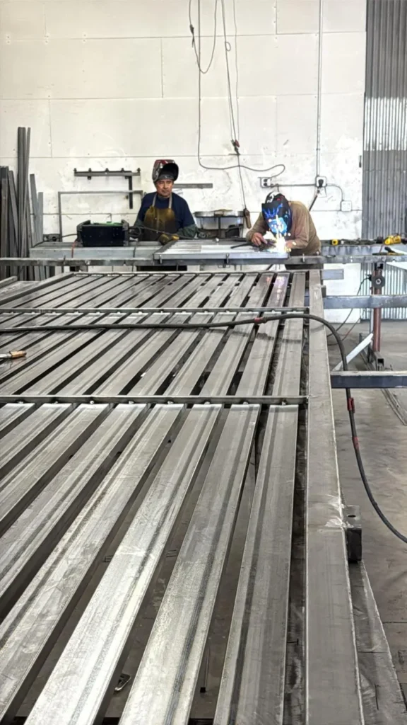 Two welders working on a large, flat metal structure.