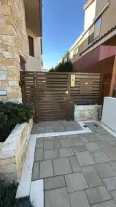 A brown horizontal metal slat pedestrian gate installed at the end of a stone-paved walkway.