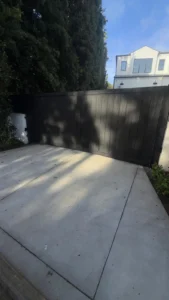 A full view of a closed matte black sliding driveway gate, providing complete privacy for a modern home.