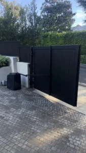 sleek, matte black privacy gate standing open over a cobblestone driveway, showcasing the automated arm and clean white concrete pillars.