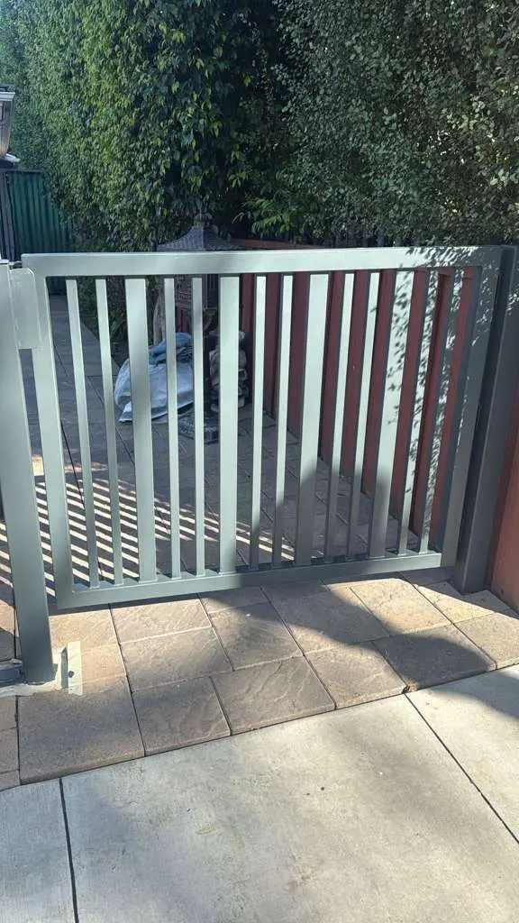 A close-up of a smaller gray metal gate with vertical slats, built into a residential perimeter fence system.