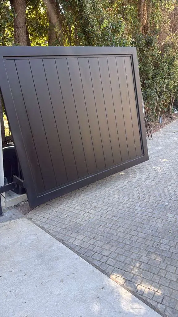 A wide-angle view of a custom-fabricated black steel sliding gate featuring vertical panels and a sleek, minimalist frame.
