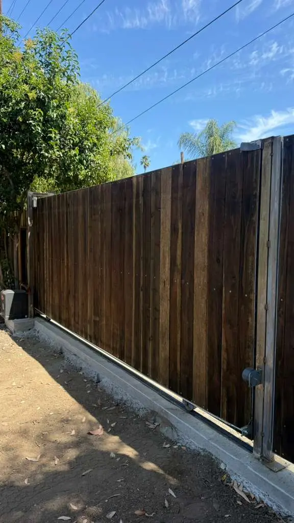 A perspective shot of a large, dark-stained sliding wooden gate installed on a concrete track along a property line.
